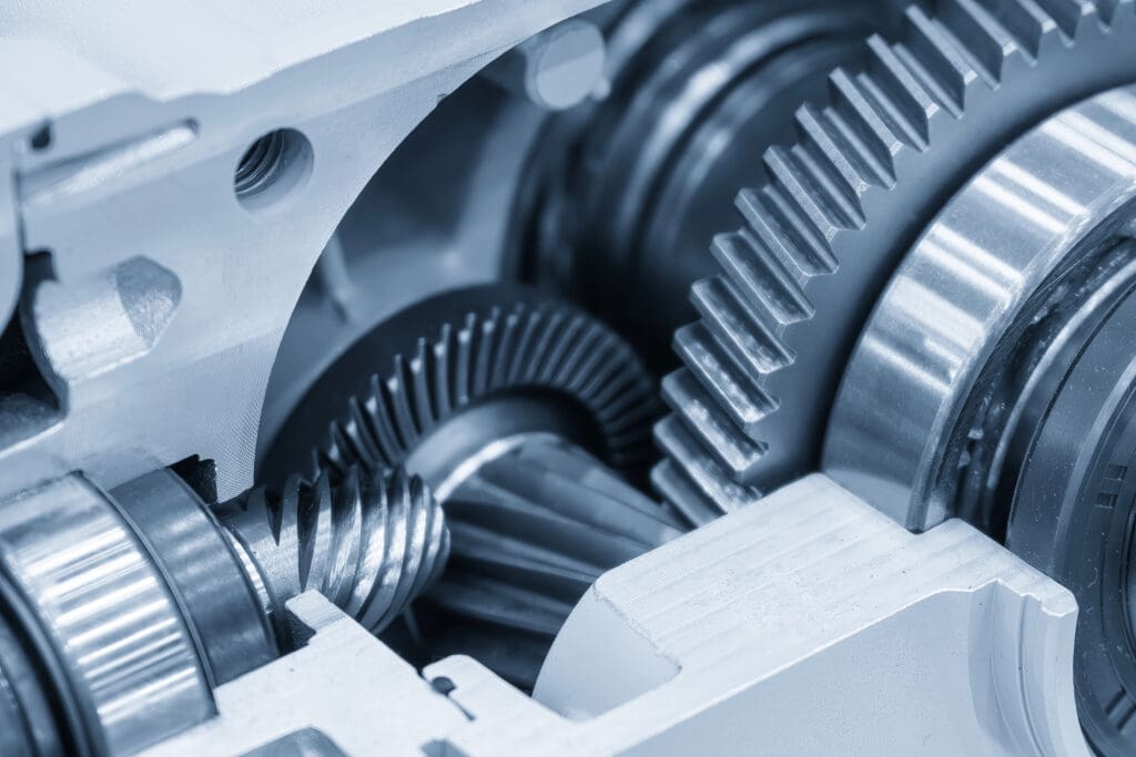 Close-up view of several interlocking metal gears inside a mechanical device, showing detailed teeth and components with a cool blue tint.