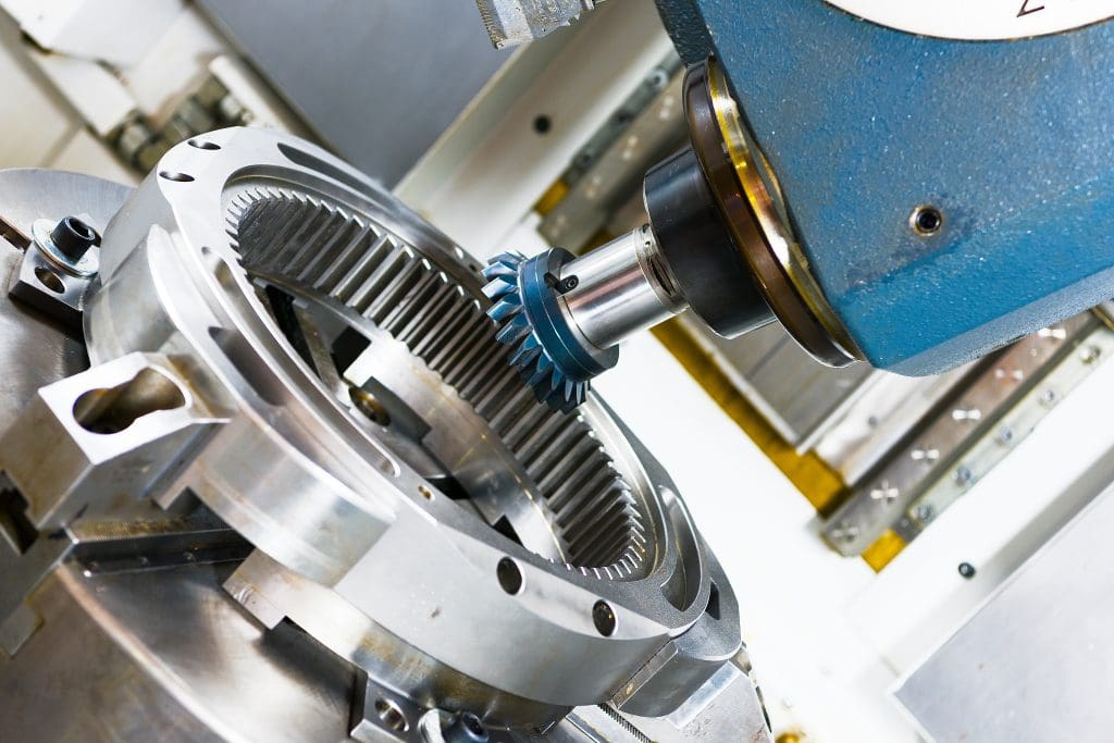 Close-up of a CNC machine milling a large metal gear, with the cutting tool engaging the inner teeth of the circular gear component in an industrial setting.