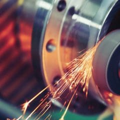 Close-up of a metal grinding process, showing sparks flying from a rotating grinding wheel as it smooths the surface of a cylindrical metal component.