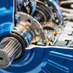 Close-up view of a metallic blue gearbox or transmission system, showing detailed gears, shafts, and mechanical components inside the cutaway housing.