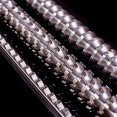 Close-up of three parallel metal machine parts with intricate grooves and ridges, set against a black background. The surfaces are shiny and reflect light, highlighting their detailed, industrial design.