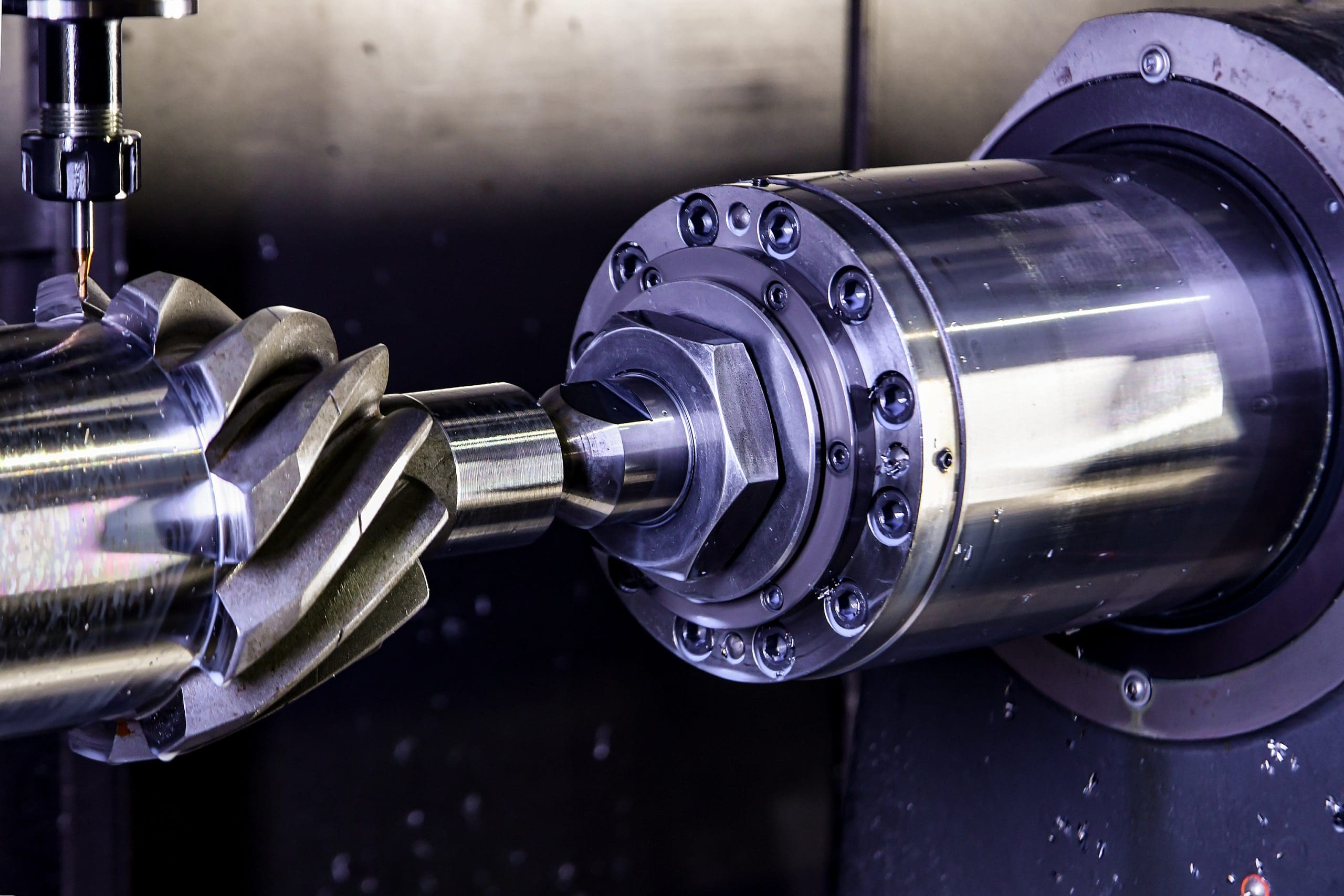 Close-up of a metal gear being machined on a CNC lathe, showing the cutting tool shaping the gear’s teeth and the shiny surface of the rotating metal part.
