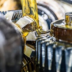 Close-up of metal gears with yellow lubricant oil being poured over them, highlighting the mechanical parts and lubrication process.