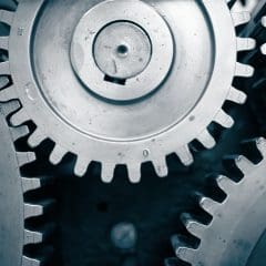 Close-up view of interlocking metal gears in a mechanical system, showing the teeth and circular shapes in a monochrome blue tone.